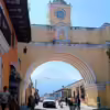 Daytime street scene featuring Arco de Santa Catalina (Saint Catherine's Arch) in Antigua Guatemala, with Volcán de Fuego seen through the arch