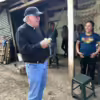 Catholic priest dressed in jeans and a baseball cap holding 4 live chicks (i.e., baby chickens) speaking with a Joya Honda family